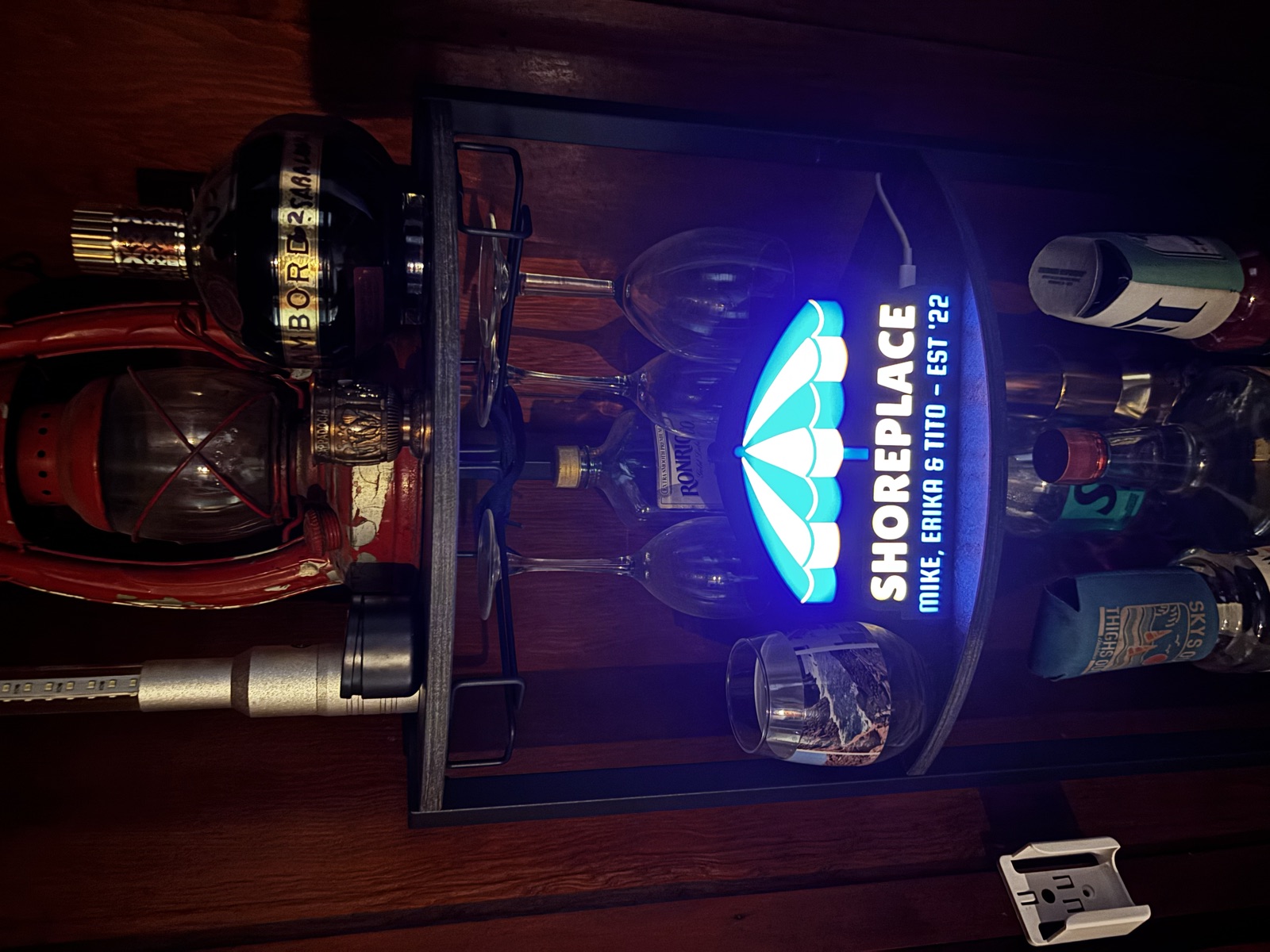 The Shoreplace lightbox glowing cyan on a corner bar cart, tucked under wine glasses.